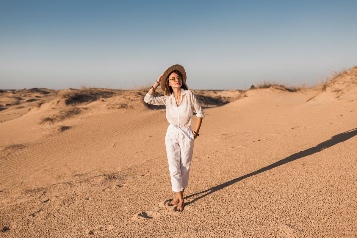 stylish beautiful woman walking in Dubai desert sand in white outfit wearing straw hat on sunset, travel safari on vacation stylish beautiful woman walking in Dubai desert sand in white outfit wearing straw hat on sunset, travel safari on vacation